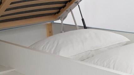 Fototapeta na wymiar Storage drawer under bed with white pillows indoors, closeup