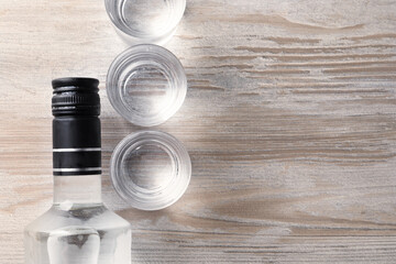 Bottle and shot glasses of vodka on wooden table, flat lay. Space for text - obrazy, fototapety, plakaty