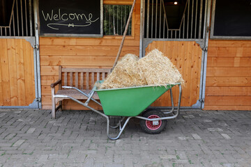 Wheelbarrow with hay near wooden stable outdoors