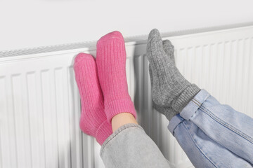 People warming feet near heating radiator, closeup