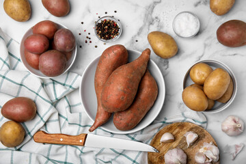 Different types of fresh potatoes on white marble table, flat lay