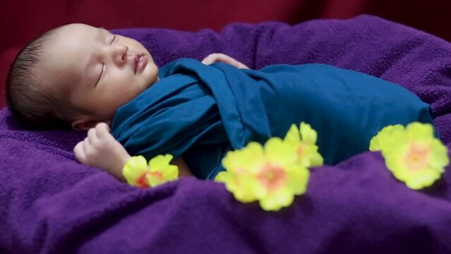 cute newborn baby sleeping in baby wrap with flowers in unique style from top angle shot