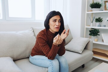 A woman looks at an engagement ring in her hand with sadness and tears, divorce and loss of a partner, breakup, unhappy heartbreak sitting at home on the couch