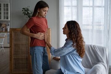 Worried concerned mother parent examining child stomach belly at home, teen girl daughter...