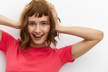Fototapeta premium a sweet, happy, funny woman in a red T-shirt with red hair color stands on a white background and holds her head with her hands, smiling happily