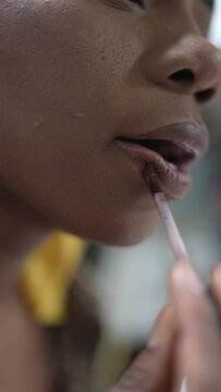 Black woman in a yellow durag applying nude lipstick