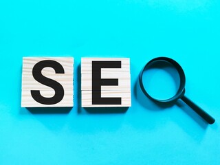 SEO concept on wooden cubes with magnifying glass against blue background.