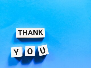 Phrase thank you on wooden cubes against aqua blue background.