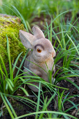 Toy brown bunny sits in the green grass, closeup. Symbol of the year 2023