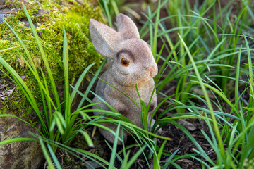 Toy brown bunny sits in the green grass, closeup. Symbol of the year 2023