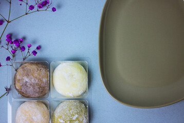 Traditional Japanese dessert mochi in rice dough or daifuku. Mochi ice cream balls and gray plate and food chopsticks on blue background flatly. Table setting, violet flowers decor. Selective focus.