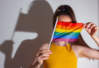 Young faceless gay woman, girl hides face behind rainbow LGBT flag. Pride Month.