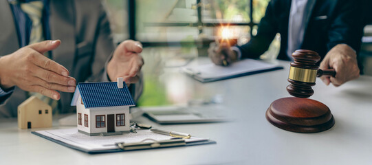 Lawyer or businessman sitting at table with fair scales Hammer and small wooden toy house work with documents Sign a contract agreement Real estate law, auction house concept