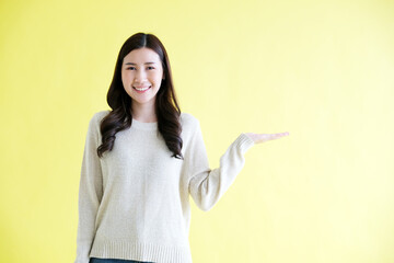 Happy young asian woman plam upplam,  for presenting product mock up, template while standing over isolated yellow background with copy space