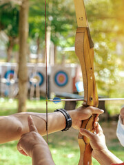 Female teacher teaches student to aim at goal. An archer teaching young man archery on field....