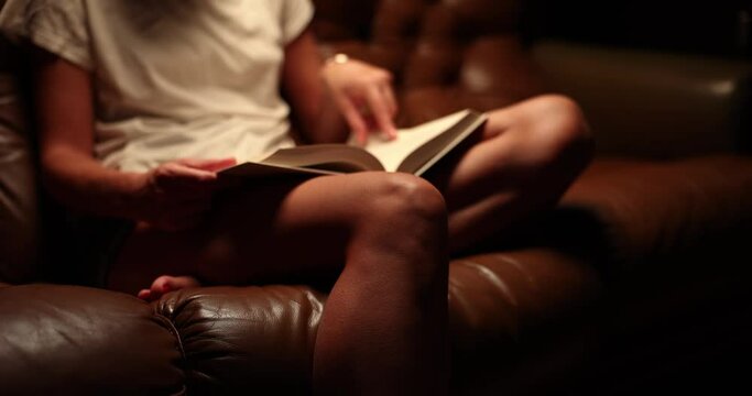 Closeup ofa woman hands sitting on sofa and reading book at home in evening