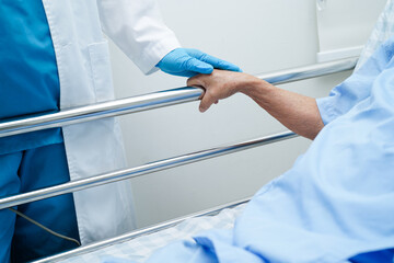 Asian elder senior woman patient holding bed rail while lie down with hope waiting her family in...