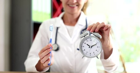 Dentist doctor holds toothbrush and alarm clock in hands during oral hygiene