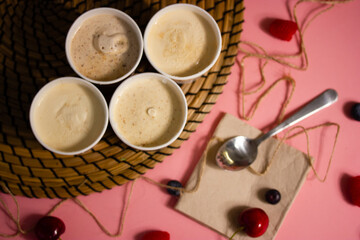Obraz na płótnie Canvas An assortment of four cans of Italian ice cream gelato stands on table, red cherries scattered on a pink tablecloth, dessert spoon. A mouthwatering, cool homemade summer dessert from rustic recipe.