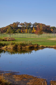 Golf course on a fall day with pond, color foliage, green grass and blue sky reflecting in the water