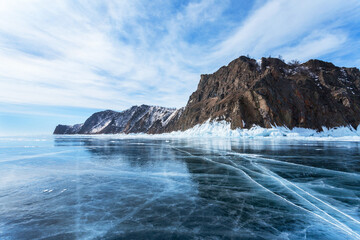 Frozen Baikal Lake on cold February day. View from clear blue ice on rocky coast of Cape Hoboy - a natural landmark of Olkhon Island. Beautiful winter landscape. Ice travel and outdoor recreation