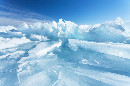 Winter natural background with fragments of blue ice and heaps of pieces of ice floes on Lake Baikal on a sunny frosty day. Abstract cold background, mock up. Harsh lifeless environment