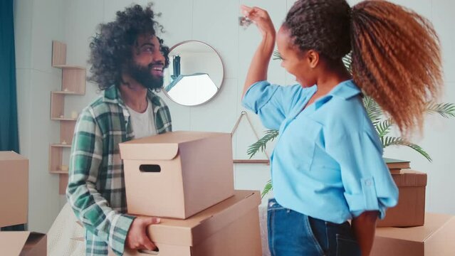 Young positive multiracial friends Arabian man and African American woman rejoice they have become homeowners hold boxes and show keys to apartment standing in new home. Rent, mortgage