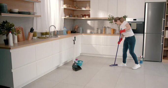 Young woman moping the floor in modern kitchen