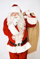 Secret, quiet and santa with christmas gift sack for silent holiday present giving in red suit. Silence of santa claus model holding festive gifts bag in studio with white background thinking.