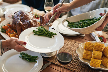 Hands, food and family at a table for thanksgiving, eating and bond on vacation, sharing a meal in their home together. Hand, vegetable and host serving woman during lunch, feast and gathering