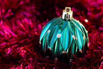 Close-up of green Christmass ball on the red tinsel garland.
