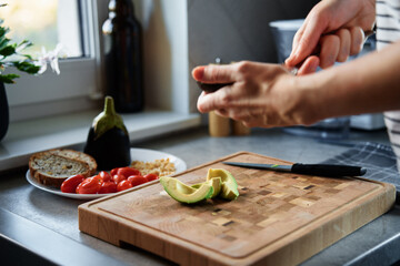 Process of woman cutting avocado for toasts in kitchen interior. Woman preparing healthy breakfast at morning. Vegan food