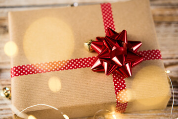 Above view of festive gift box wrapping in craft paper with festive ribbons and bow. Present for Christmas holidays on wooden background with bokeh lights