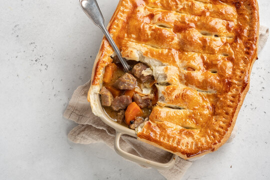 English beef steak stew pie with crispy puff pastry in a baking dish on the table