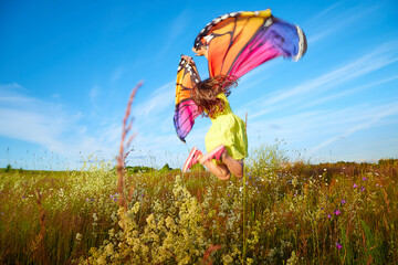 Beautiful little girl in yellow dress and in colorful bright butterfly wings in the field with...