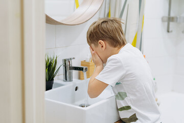 cute 6 years old boy washing his face over the sink in bathroom. Image with selective focus