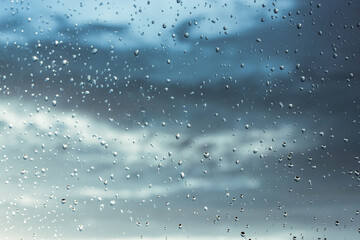 Window, raindrops on surface against blue cloudy sky after storm. Rainy weather.