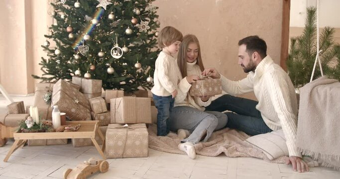 Family in sweaters unpacking christmas gifts near decorated tree