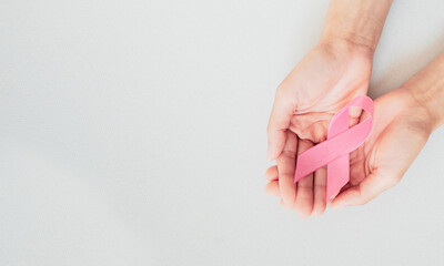 Woman's hands holding pink ribbon on white cloth background. Symbol of breast cancer awareness campaign. Healthcare concept