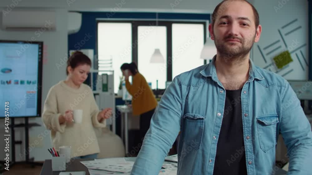 Poster portrait of confident man entering frame posing with arms crossed and smiling in busy startup office