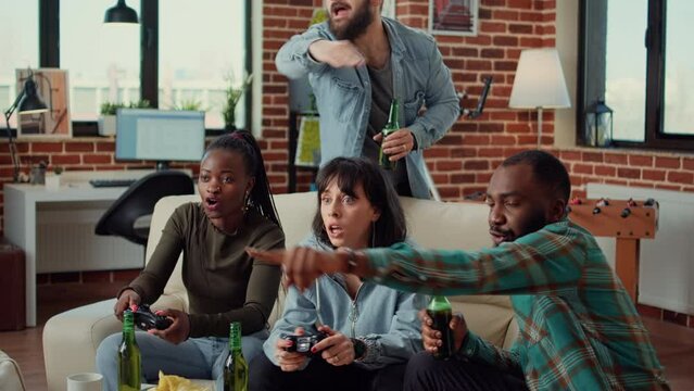 Group of friends playing video games on television console, having fun with gaming competition online at home gathering. Cheerful people meeting to play game on tv, drinking beer.