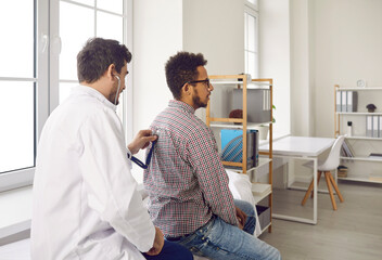 During medical appointment doctor listens to patient's lungs with stethoscope for wheezing. Young...