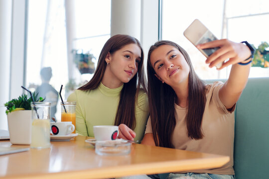 Women friends on coffee break at cafeteria using mobile phone