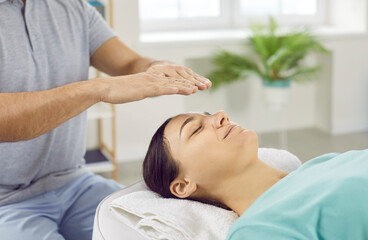 Happy young woman regaining energy while relaxing on bed during therapy session with professional Reiki healer. Holistic treatment, spiritual therapy, Reiki healing concepts