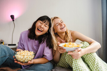 Two multiracial girls eating snacks while watching movie together