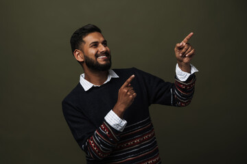 Portrait of young positive indian man pointing upper right corner