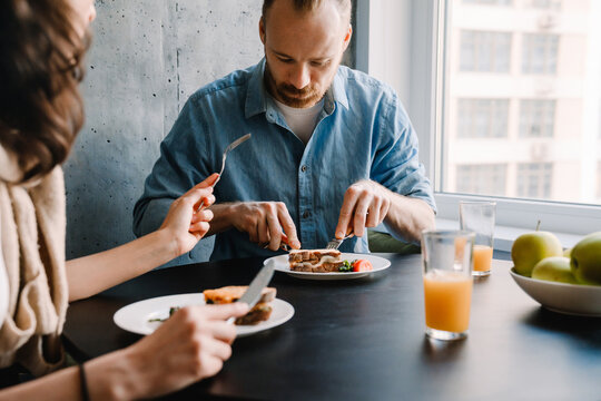 Young white couple sitting by table while having breakfast at home