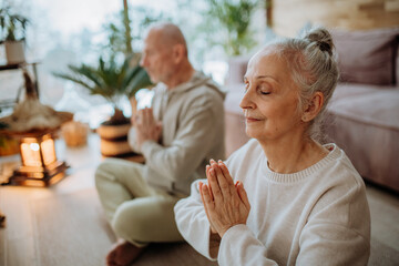 Senior couple meditating together in their living room during cold autumn day.