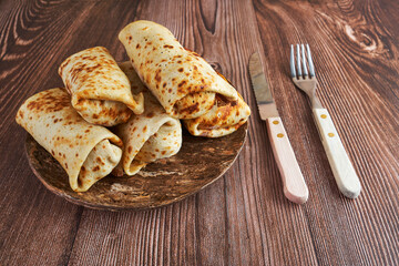 fork, knife and stuffed pancakes on a clay plate, rustic style