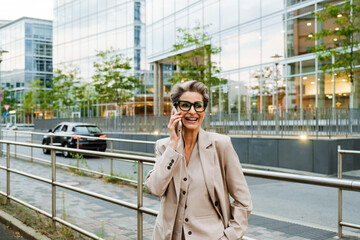 Fototapeta premium Mature grey woman talking on cellphone while standing on city street